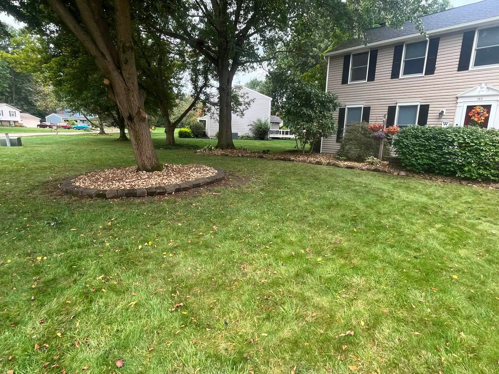 Paver-edged stone ring under a mature shade tree, lawn cut and edged to the walk